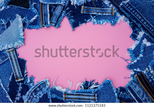 Denim frame from Lots of little ripped pieces of\
denim jeans fabric on pink leather background. Ripped Destroyed\
Torn Denim Frame, copy\
space