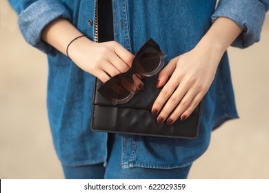 Denim outfit fashion details  Stylish woman and red glitter manicure in navy jeans holding sunglasses   leather small cross body bag 