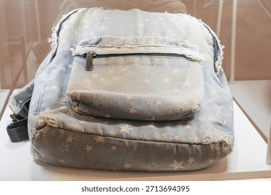 Denim patchwork backpack, American flag design, display case, museum setting, worn condition, frayed edges, large hole, denim straps, soft shadows, vintage look, still life photograph