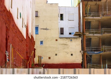 Dense, Chaotic Residential Buildings In The Old Quarter Of The City Behind A Fence. Construction Or Reconstruction Of A House. Red, Yellow And White Building Facades Background. Urbanization Concept.