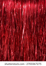 A dense, close-up view of numerous thin, vertical strands of shiny red tinsel.