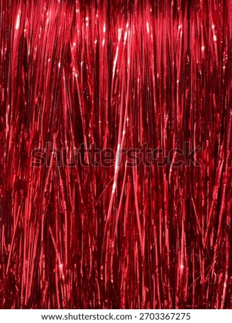 A dense, close-up view of numerous thin, vertical strands of shiny red tinsel.