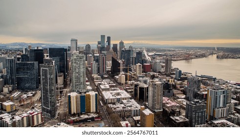 A dense cluster of skyscrapers forms a dynamic cityscape, with snowy mountain peaks visible in the background. The buildings varied heights and modern designs create a visually engaging foreground.