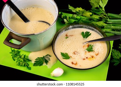 Dense Creamy Cauliflower Soup In Plate And Pot, Spilled Soup On Green Kitchen Board And Parsley Leaf, All On Black Background.