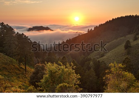 Dense fog rolls in over the Pacific Ocean at sunset over coastal California mountains