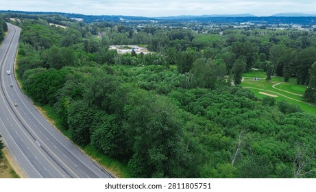 Dense forest canopy frames residential cul de sacs near Kent Des Moines Road arterial pathways. Wide angle perspective displays natural buffer zones separating living quarters from primary. USA
