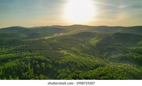 Dense forest and mountainous terrain at dawn from a bird's-eye view. Sunlight illuminates the area. Bright sun. - Powered by Shutterstock