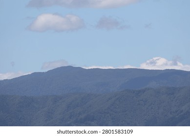 dense, forested mountain range under partially cloudy blue sky (wide-angle, panorama, landscape)