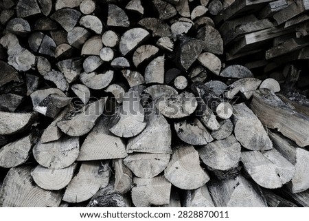 A dense, full-frame texture shot of chopped, split wooden logs and tree branches stacked neatly together in a storage pile for winter heating fuel.