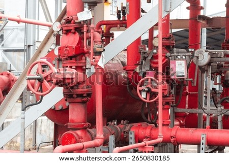 A dense network of red pipes, valves, and gauges part of a fire suppression or industrial fluid transfer system, in an outdoor setting.