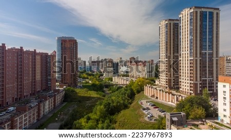 Dense trees growing along the river in a big city. Photograph of the Eltsovka River in Novosibirsk. High-rise buildings built near the river. Photos of Novosibirsk, Russia, Autumn cityscape