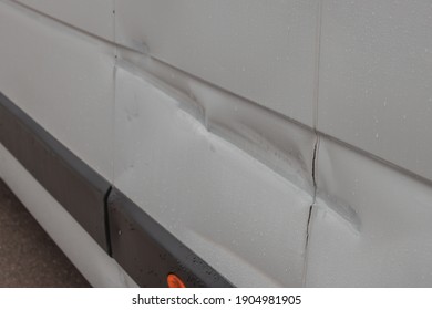 Dent Or Destroyed Bent Panel Of A Panel Van. Delivery Or Other Common Van Being Hit On A Sidepanel. Minor Damage To A Body Panel Of A White Van.