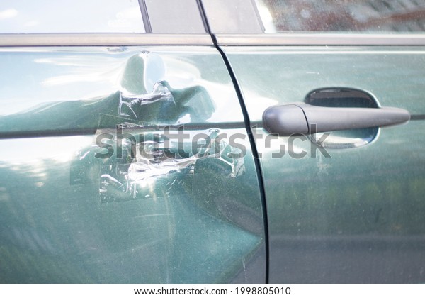 A dent on the car door.\
Damaged transport. A wrecked car. The side door is damaged by a\
blow.