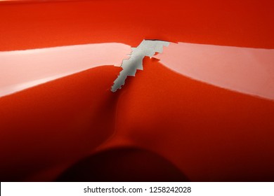 dent on red painted metal. background loose paint on metal. dent on car close up.