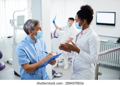 Dental Assistant Taking Notes While Communicating With Black Female Dentist At Dental Clinic. 