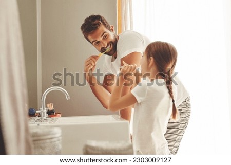 Dental care, father with daughter brush their teeth and in bathroom of their home. Oral hygiene routine, parent with child use toothbrush for health and wellness mouth protection in the morning