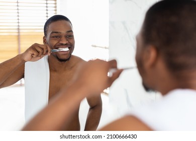 Dental Care. Handsome Shirtless Black Guy Brushing Teeth Near Mirror In Bathroom, Happy Young African American Man Making Morning Hygiene At Home, Smiling To His Reflection, Selective Focus