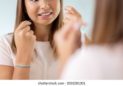 Dental Care, Hygiene And People Concept - Happy Smiling Teenage Girl With Floss Cleaning Teeth And Looking In Mirror At Bathroom