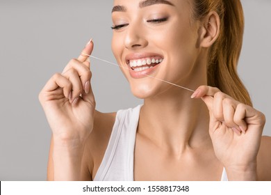 Dental care. Young woman using dental floss over grey studio background - Shutterstock ID 1558817348