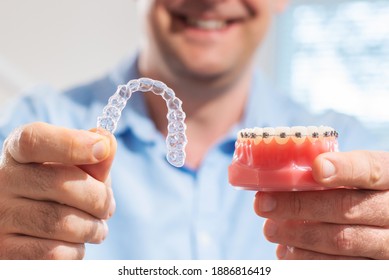 Dental care.Smiling dentist doctor holding aligners and braces in hand shows the difference between them - Shutterstock ID 1886816419