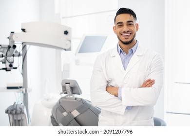 Dental Center. Portrait Of Smiling Middle Eastern Dentist Doctor Posing At Workplace, Handsome Arab Stomatologist Standing With Folded Arms In Modern Clinic Interior, Ready For Check Up With Patient