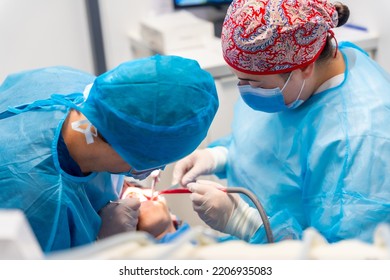 Dental clinic, women dentists in blue suits and hats performing an oral operation