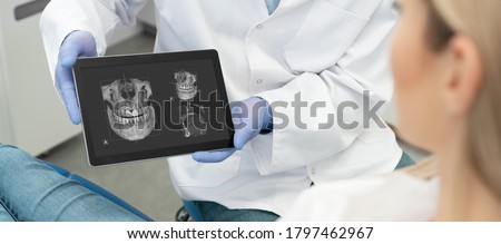 Dental consultation in clinic. Dentist showing teeth x-ray on digital tablet screen. 3D tomography technology.