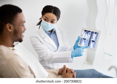 Dental Consultation Concept. Black Female Dentist Showing Teeth X-ray On Digital Tablet Screen To Male Patient, Professional Stomatologist Consulting Young Man About Teeth Treatment, Closeup - Powered by Shutterstock