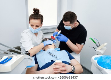Dental Curing Light: Polymerization Process. Dentist and assistant applying filling to patient's tooth in modern dental clinic. Teamwork in Dentistry.