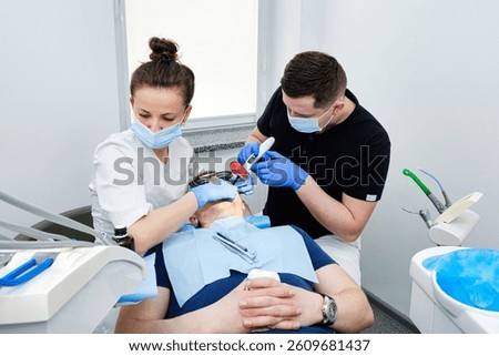 Dental Curing Light: Polymerization Process. Dentist and assistant applying filling to patient's tooth in modern dental clinic. Teamwork in Dentistry.