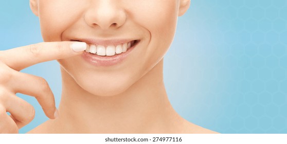 Dental Health, Beauty, Hygiene And People Concept - Close Up Of Smiling Woman Face Pointing To Teeth Over Blue Background