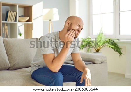 Dental health problems concept. Man suffering from strong toothache. Upset male patient with inflamed nerve, tooth abscess, or teeth sensitivity sitting on sofa and touching cheek with grimace of pain Stockfoto © 