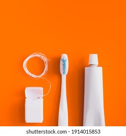 Dental hygiene objects: toothbrush, toothpaste and floss. White generic accessories for keeping teeth health in bright orange backdrop