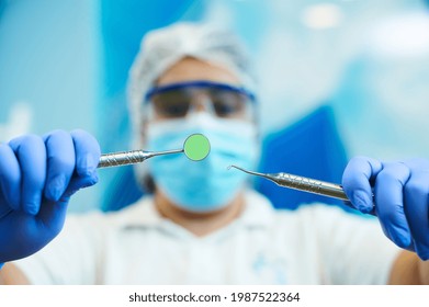 Dental Instruments In The Hands Of A Blurred Female Dentist Doing Dental Examination On A Blurred Blue Background