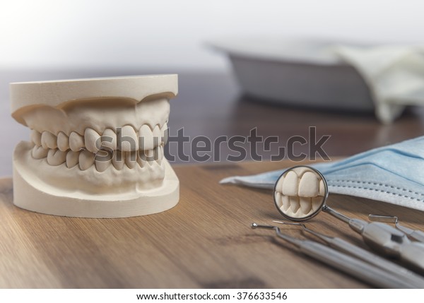 Dental mold of a set of false teeth\
with dental tools on a wooden table arranged so that the mirror\
reflects the teeth in a dentistry and healthcare\
concept