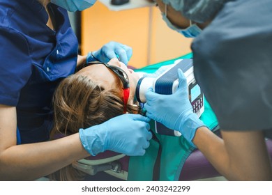 Dental portable tooth X-ray. Little scared girl sitting in chair in dentist doctor office in protective safety sunglasses. Kid,child afraid of teeth extraction, treatment. Open mouth. Clinic check-up. - Powered by Shutterstock