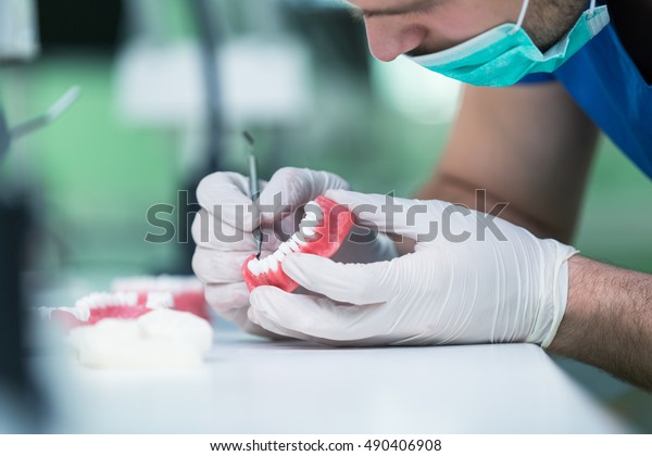 Dental prosthesis, dentures, prosthetics\
work. Prosthetics hands while working on the denture, false teeth,\
a study and a table with dental\
tools.
