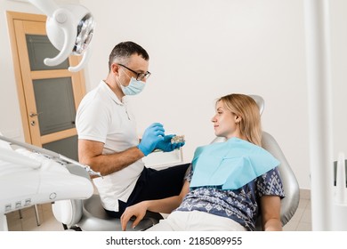 Dental prosthetics consultation with dentist for patient woman in dentistry. Doctor dentist shows artificial plastic jaw with dental implants - Shutterstock ID 2185089955