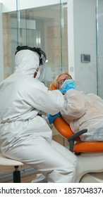 Dental Specialist With Coverall Talking With Senior Patient Before Examination During Pandemic Covid-19. Concept Of New Normal Dentist Visit In Coronavirus Outbreak Wearing Protective Suit And Face