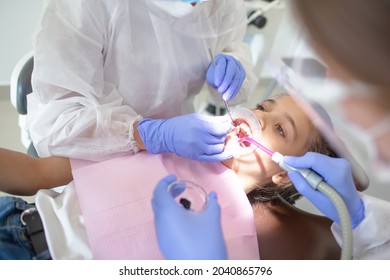 The Dental Surgeon Makes The Oral Examination Of Mouth To Female Child In The Dental Office. The Young Girl Sit In Dental Chair With Open Mouth During The Doctor's Examination