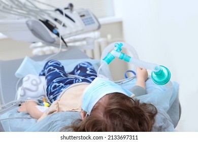 Dental Surgery Under General Anesthesia. The Child Is Under Anesthesia. A Mask With Oxygen On The Child's Face. The Child Is Out Of Focus.