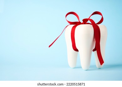 Dental treatment concept. Dental offers free treatment. White tooth model with red bow ribbon on a blue background with copy space, close-up - Shutterstock ID 2220515871