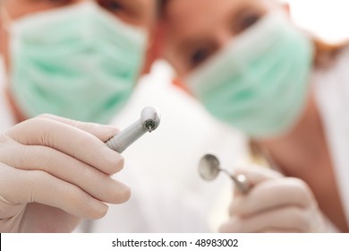 dental treatment with dentist and dental assistant bowing over the patient as seen from patient's perspective. They have drills and angled mirrors, focus on tools
