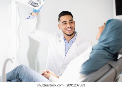 Dental Treatment. Portrait Of Middle Eastern Dentist Doctor Having Check Up With Muslim Female Patient In Modern Clinic, Friendly Arab Stomatologist Man Turning On Lamp And Smiling, Close Up