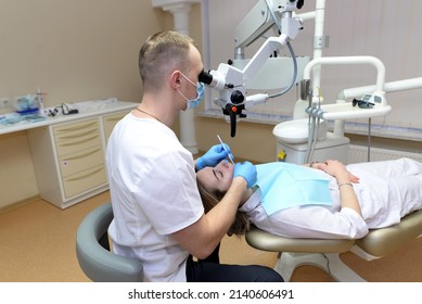 Dental Treatment Under A Microscope. Male Dentist Treats Teeth Using A Microscope In A Dental Clinic