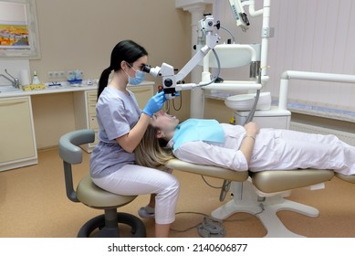 Dental Treatment Under A Microscope. Woman Dentist Treats Teeth Using A Microscope In A Dental Clinic