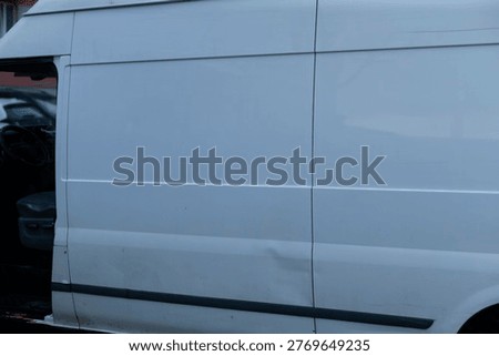 Dented side panel of van closeup, metal crease and paint scuff detailed, reflection of apartment facade, focus on damage and repair needs, insurance documentation imagery potential