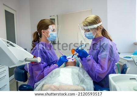 Dentist and assistant in blue latex gloves and masks fill the teeth of his patient in goggles. The concept of dental treatment