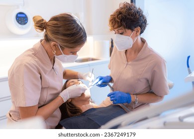 Dentist and assistant examining the mouth of a patient lying on the chair of a clinic - Powered by Shutterstock