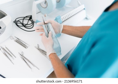 Dentist assistant sterilizing and packing dentist equipment in plastic sterilization pouches - Shutterstock ID 2136956171